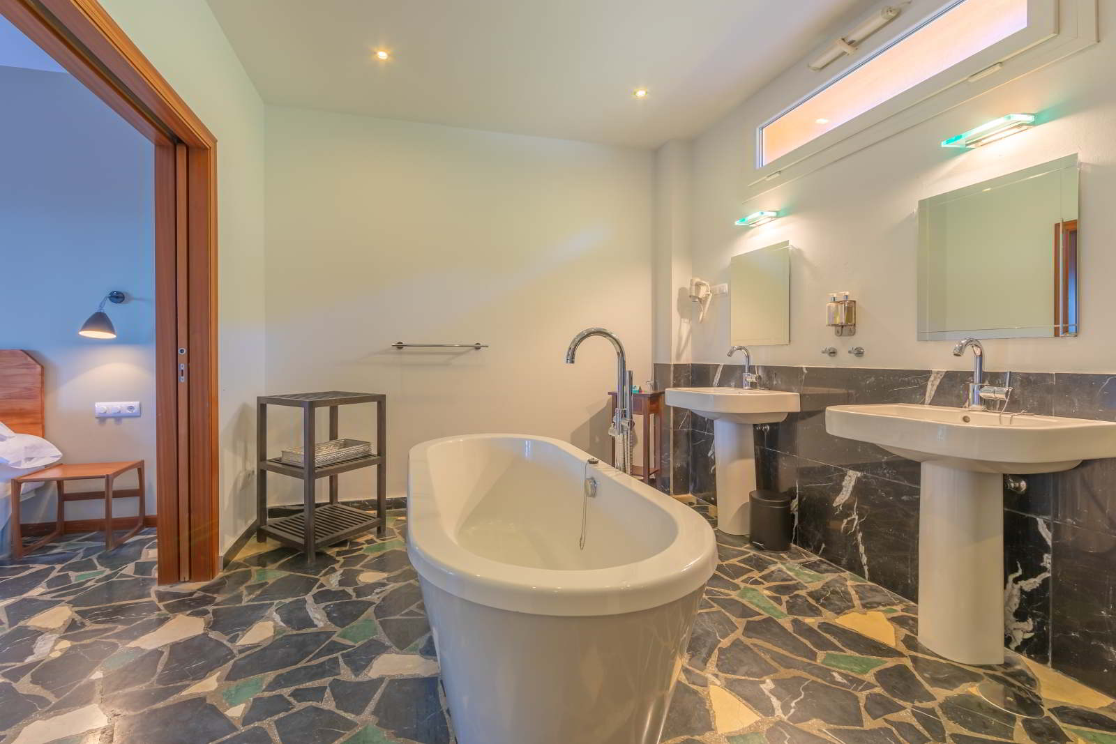 Baño de habitación junior suite con bañera exenta, doble lavabo, griferia moderna y suelo de piedra natural en el Hotel Punta Sur.