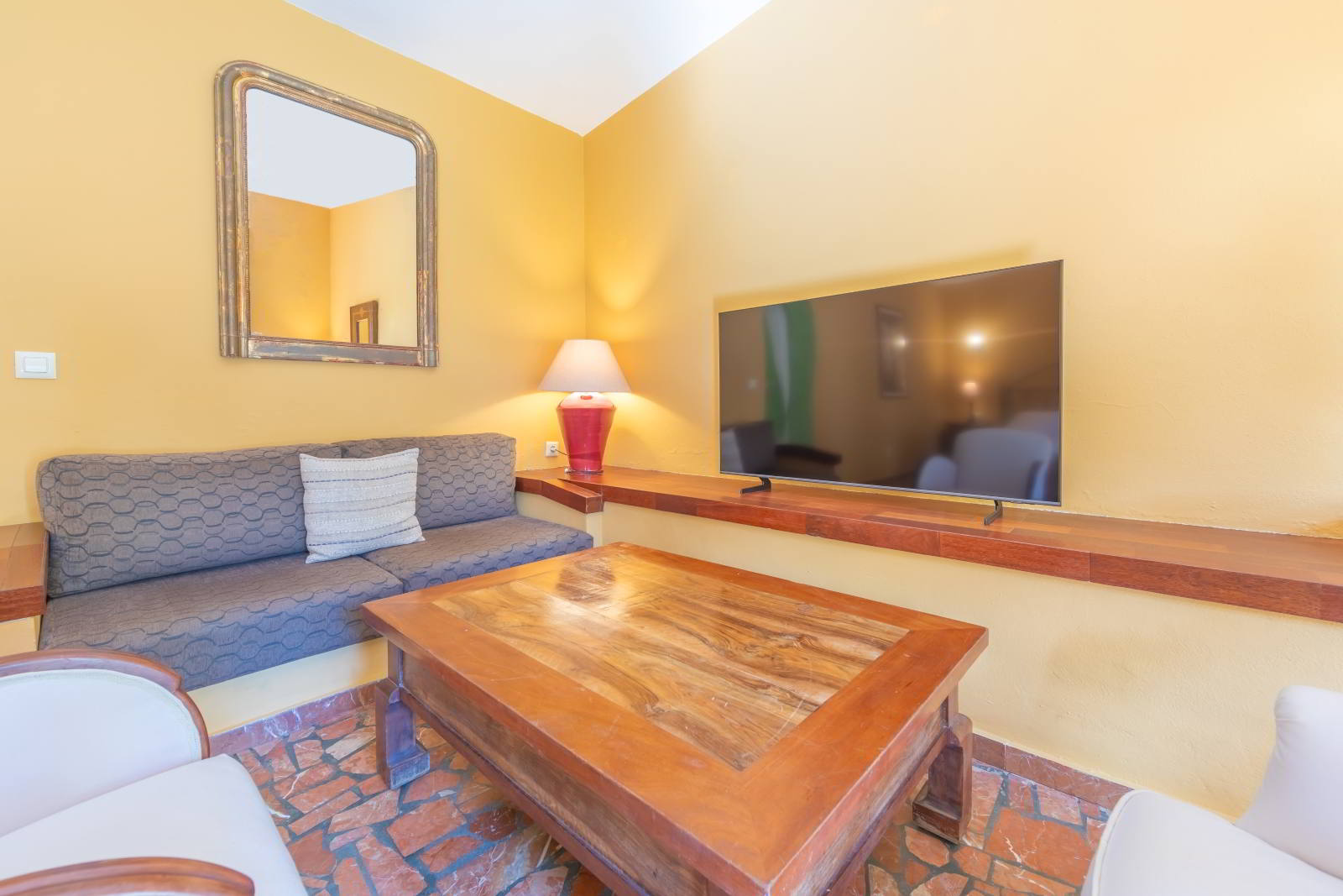 Rincón de estar de habitación familiar con sofá, mesa de centro de madera, televisión y luz cálida en ambiente acogedor.